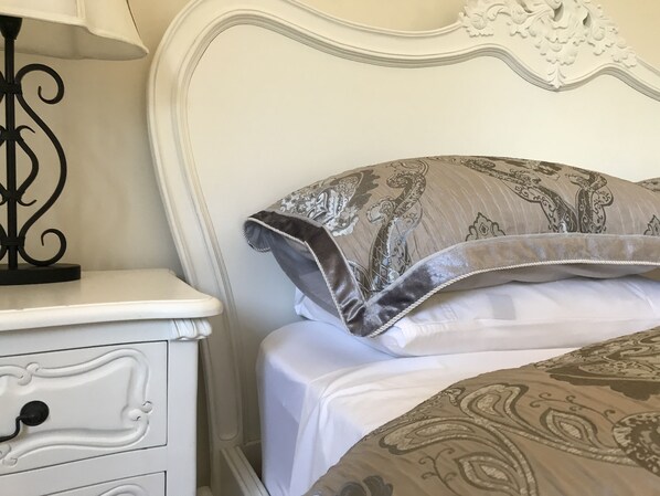 A bed with patterned pillows and a white nightstand with a lamp. - Velvet Pear Cottage @ The Foxglove Gardens (Tilba Tilba)