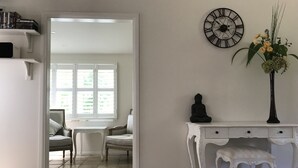 Una habitación con un escritorio blanco, una estatua de Buda negra, un reloj y un florero con flores.