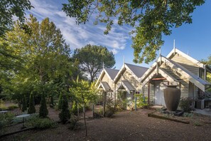 A building with a traditional architectural style, featuring a prominent chimney and a large decorative urn in the garden. - Velvet Pear Cottage @ The Foxglove Gardens (Tilba Tilba)