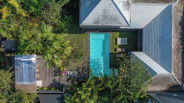 Vue aérienne d’une propriété dotée d’une piscine, entourée d’une végétation luxuriante et d’une terrasse en bois.