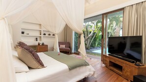 Ein Schlafzimmer mit Bett, Fernseher, einem Holzschrank und einem Balkon mit Blick auf Grünflächen.