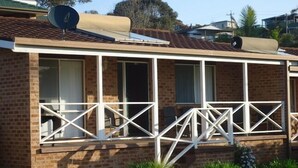 Une maison en briques avec un balcon, une antenne parabolique et un petit jardin.