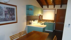 Une cuisine compacte avec une table et des chaises en bois, un petit îlot central doté d’un évier et un réfrigérateur.