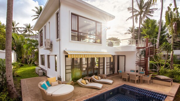Una casa moderna de dos pisos con piscina, mobiliario exterior y una escalera en espiral.