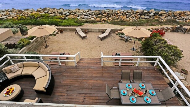 A wooden deck with a curved sofa, a dining table with chairs, and two umbrellas.