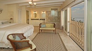 A bedroom with a bed, a chair, a vanity with a mirror, and a view of the ocean through a sliding door.