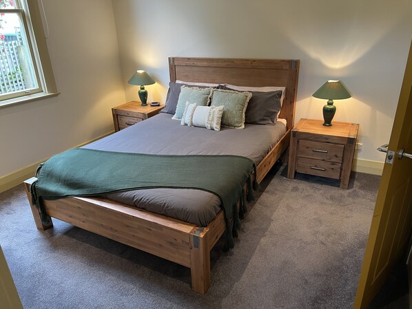 Une chambre à coucher avec un lit en bois, deux tables de chevet, un plaid vert et deux lampes.