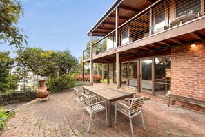 A two-story building with a brick exterior, a wooden deck, and a table with chairs. - Bay Vista (Lorne)
