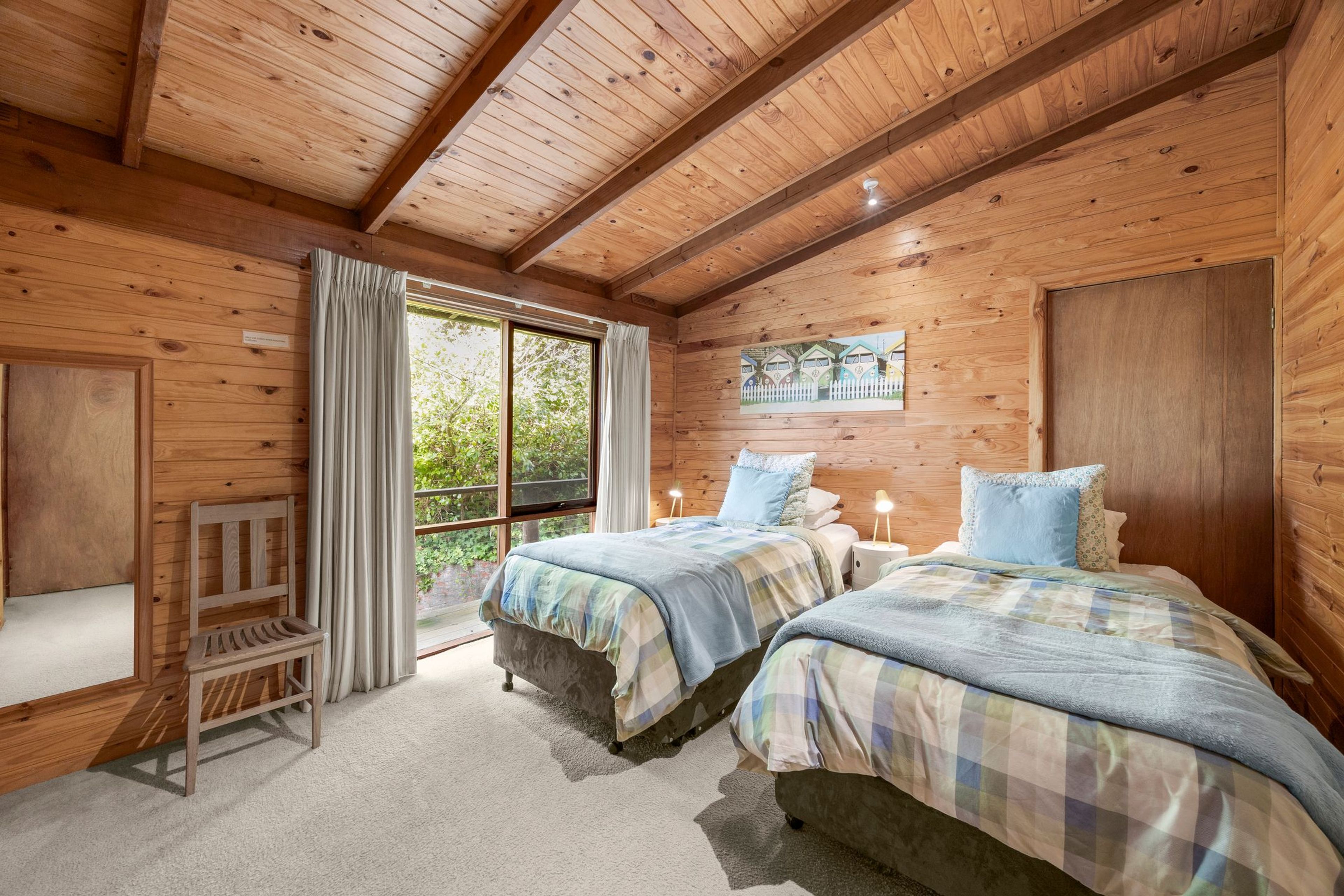 A wooden cabin bedroom with two beds, a bench, and a large window.