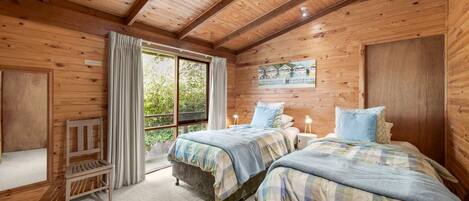 A wooden cabin bedroom with two beds, a bench, and a large window.