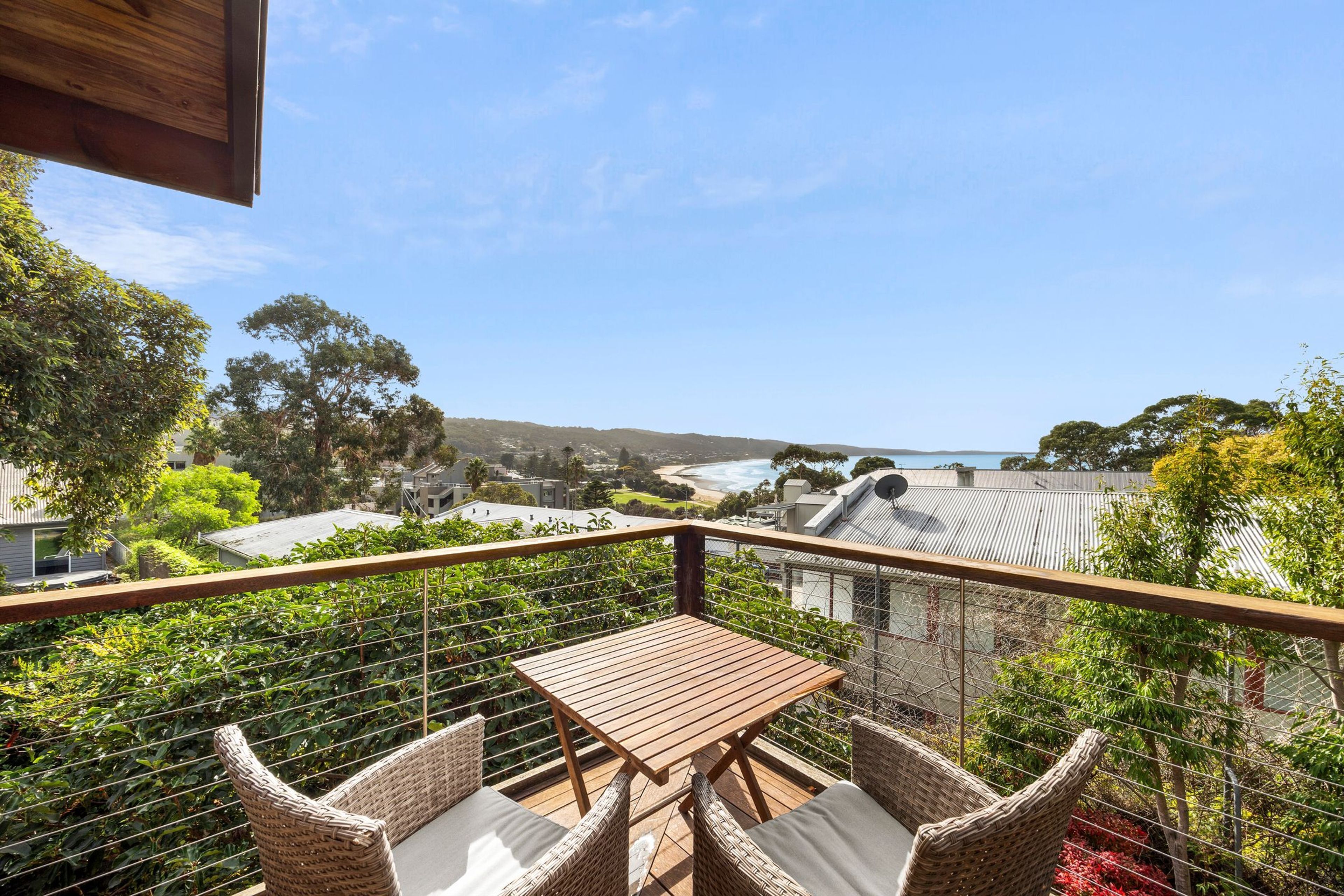 Un balcon avec une table et des chaises, donnant sur un paysage côtier avec des maisons et une plage.