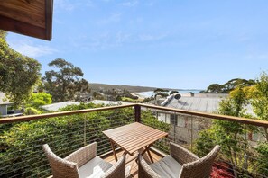 A balcony with a table and chairs, overlooking a coastal landscape with houses and a beach.