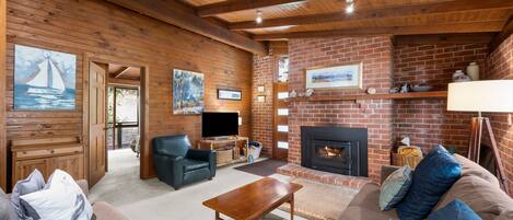 A cozy living room with a fireplace, wooden walls, and a television.