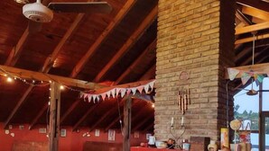 An indoor dining area with a brick fireplace, wooden ceiling beams, and string lights. - Hostería Las Grullas (Villa Gesell)