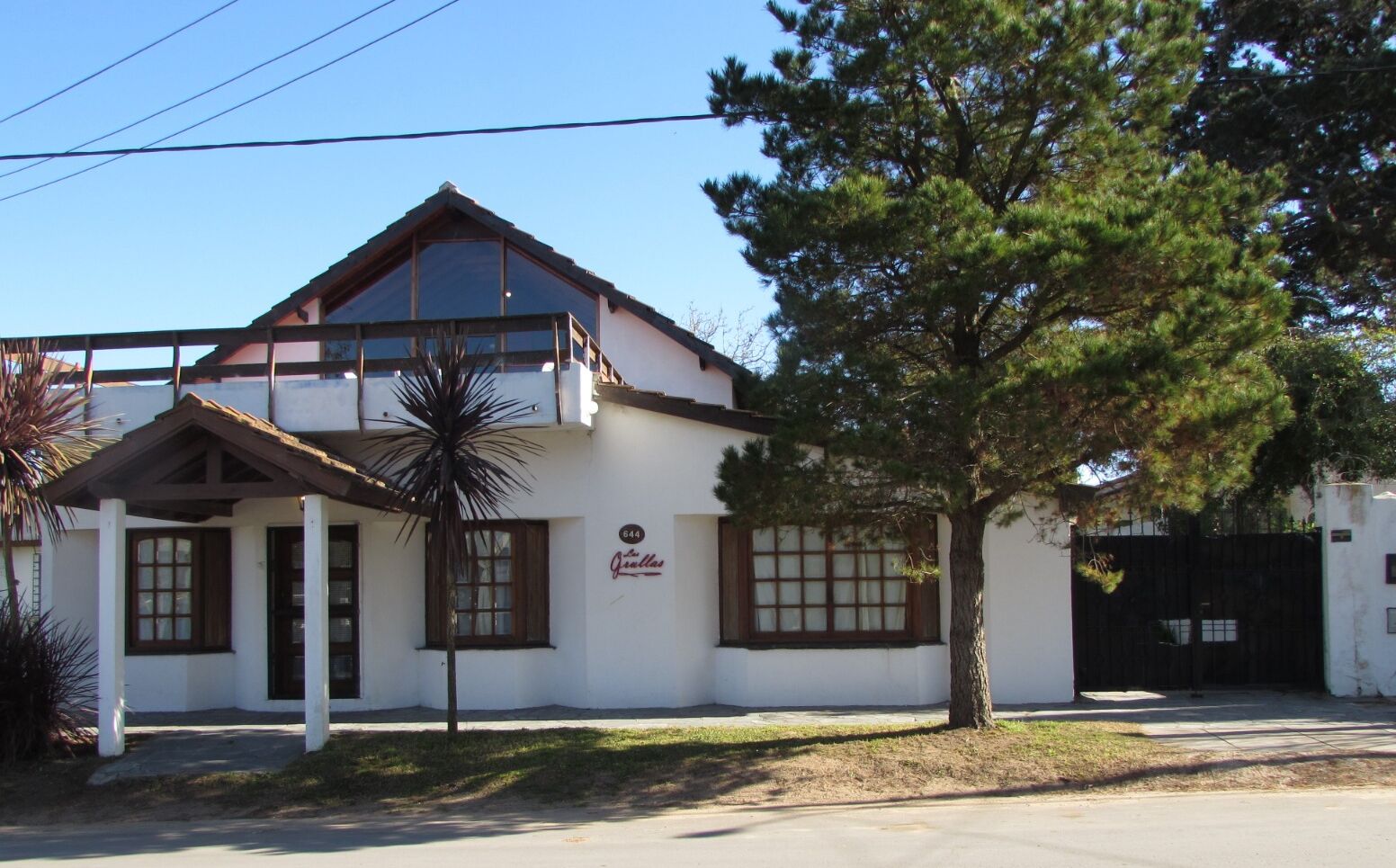 A two-story building with a white facade, a brown roof, and a sign that reads "Jardines."