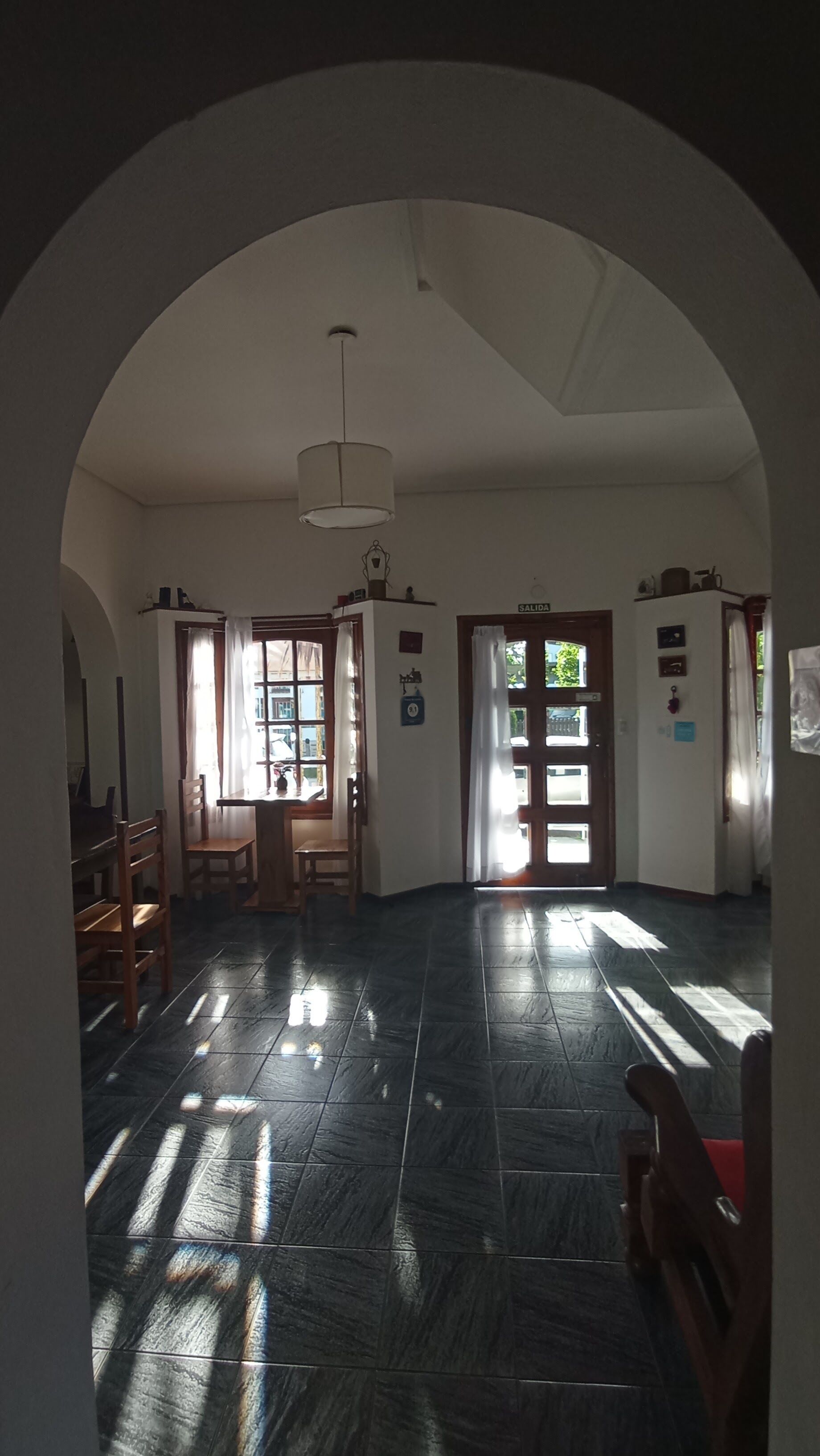 Una stanza spaziosa con pavimento piastrellato, un tavolo di legno, sedie e una lampada a soffitto.