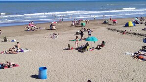 A beach with people sunbathing, tents, and a surfboard. - Hostería Las Grullas (Villa Gesell)