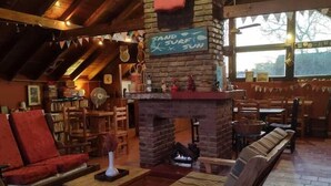 A cozy interior with a stone fireplace, wooden furniture, and a view of the outdoors. - Hostería Las Grullas (Villa Gesell)