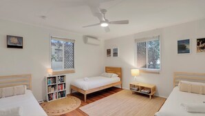 Ein Schlafzimmer mit zwei Einzelbetten, einem Deckenventilator und einem großen Fenster mit Jalousien.
