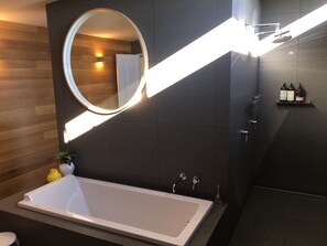 A modern bathroom with a large bathtub, a round mirror with integrated lighting, and a shower area. - Signature on Gunn. Devonports finest executive holiday home. (Devonport)