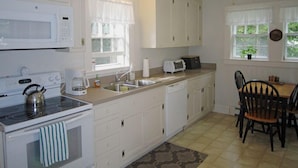 A kitchen with white cabinets, a stove, a microwave, a sink, and a ceiling fan. - 4BR Cape Style Near Saints Landing and Paines Creek (2086) (Brewster)