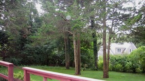 A wooden deck with a red railing overlooking a grassy area with trees and a house in the background. - 4BR Cape Style Near Saints Landing and Paines Creek (2086) (Brewster)