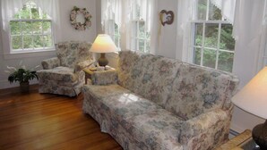 A cozy living room with floral-patterned furniture, a lamp, and a wreath on the wall. - 4BR Cape Style Near Saints Landing and Paines Creek (2086) (Brewster)