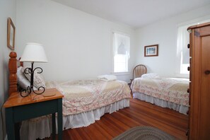 A bedroom with two single beds, a nightstand, a chair, a wooden wardrobe, and a window with curtains. - 4BR Cape Style Near Saints Landing and Paines Creek (2086) (Brewster)