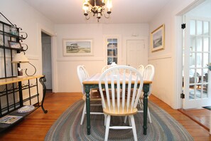 A dining area with a table set for four, surrounded by white chairs, a chandelier, and framed artwork on the walls. - 4BR Cape Style Near Saints Landing and Paines Creek (2086) (Brewster)