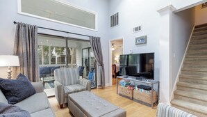 A spacious living room with a large TV, comfortable seating, and a staircase.