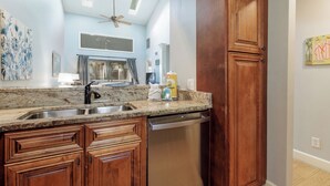 A kitchen with wooden cabinets, a granite countertop, a dishwasher, and a ceiling fan. - 7304 Treetops: South Forest Beach Villa. Free Bikes, Near Beach, Pool! (Hilton Head Island)