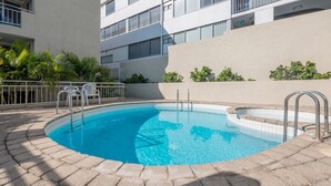 Une piscine dont le bord est revêtu de carreaux, entourée d’un chemin pavé en briques. Des chaises et une rambarde en métal sont disposées le long du bord de la piscine.