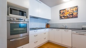 Une cuisine moderne dotée d’appareils électroménagers en acier inoxydable, de meubles blancs et d’un tableau représentant des pâtisseries, accroché au mur.