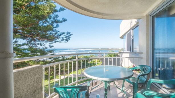 Un balcon avec vue sur l’océan, une table ronde et deux chaises.