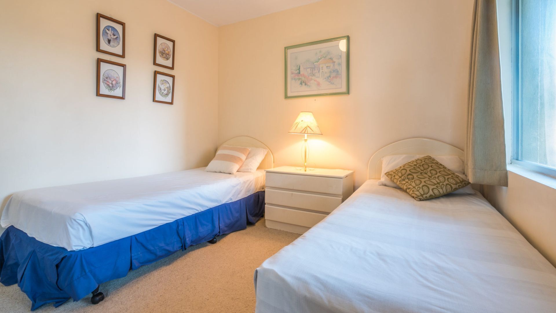 Une chambre double avec deux lits, une table de chevet, une lampe et un tableau au mur.