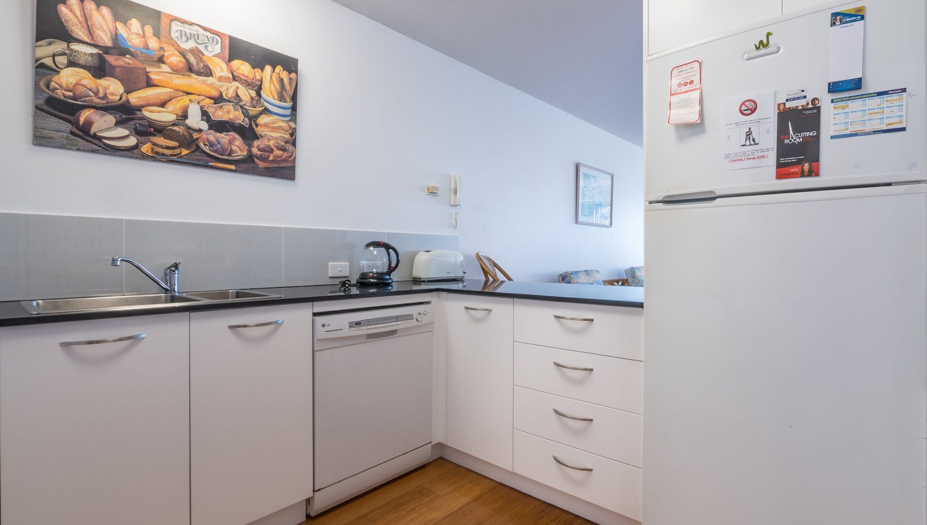 Een moderne keuken met witte kastjes, een zwart aanrecht, een koffiezetapparaat en een koelkast met magneetjes en briefjes.