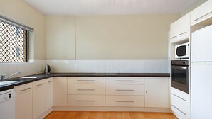 A modern kitchen with white cabinets, a black countertop, a stainless steel kettle, a built-in oven, and a microwave. - Sunrise Court 3 - Bilinga/ North Kirra Beachfront (Bilinga)