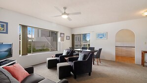 A modern living room with a sofa, armchairs, a dining table, and a kitchen area visible through an archway. - Sunrise Court 3 - Bilinga/ North Kirra Beachfront (Bilinga)