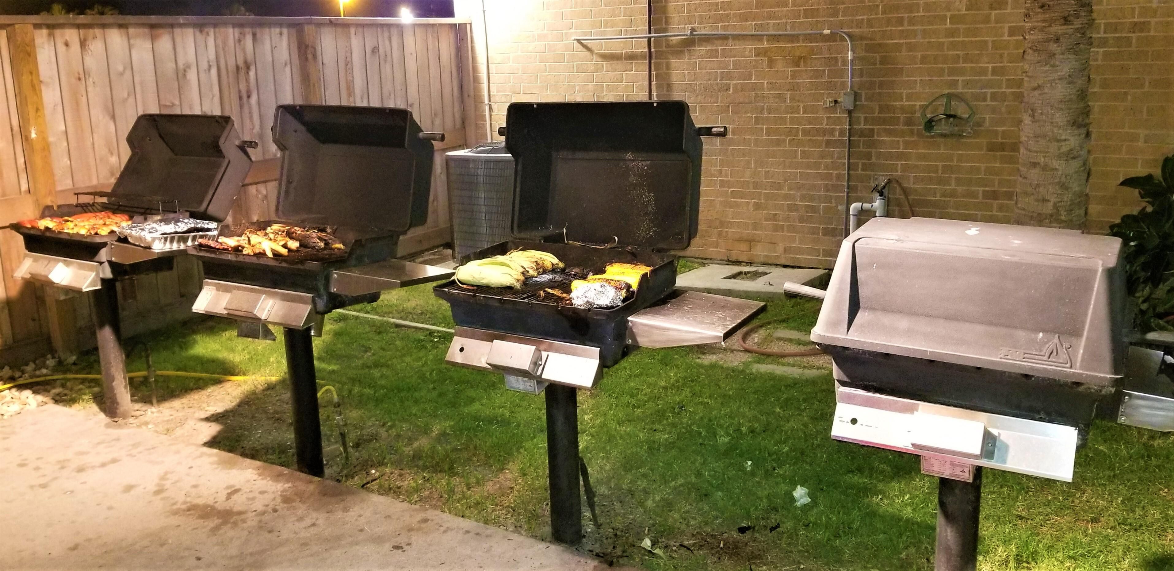 A backyard with three barbecue grills, a brick wall, and a wooden fence.