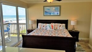 Un dormitorio con cama, dos lámparas de noche, una mesita de noche, una ventana con vista a la playa y un ventilador de techo.