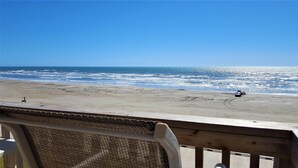 Vista a la playa desde una terraza de madera con una silla al frente.