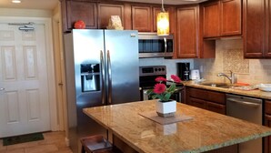 Una cocina con armarios de madera, electrodomésticos de acero inoxidable, encimera de granito y una pequeña isla decorada con un florero.