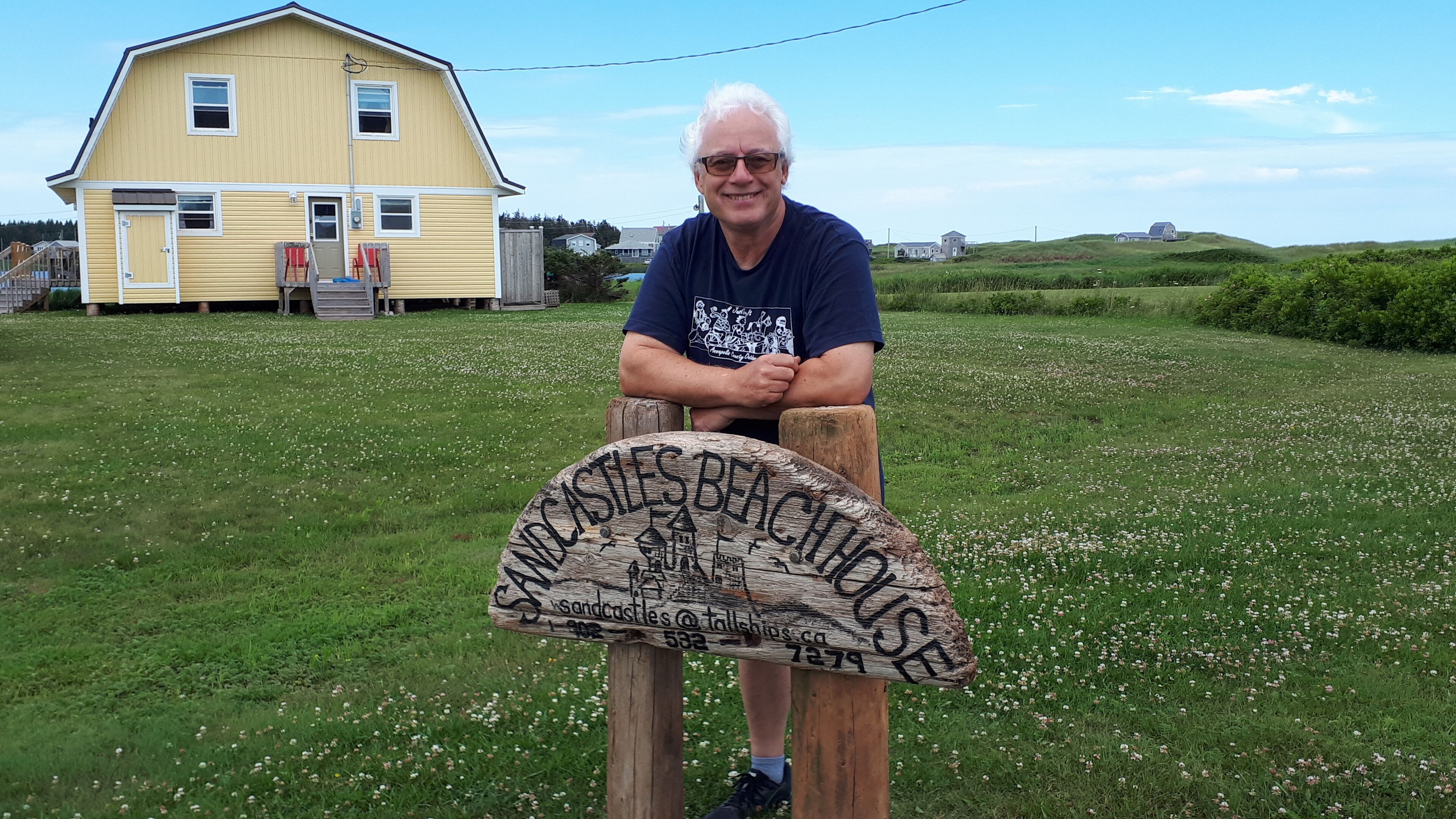 A man sitting on a wooden bench in front of a sign that reads "Sandcastles Beach House."