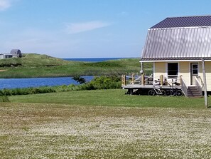 A house with a metal roof, a porch with a table and chairs, and a bicycle parked outside. - Sandcastles Beach House - Meadowside: On PEI's Best Beach! (Kensington)
