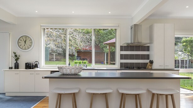 A modern kitchen with a large island, bar stools, a clock, and a view of the backyard. - Spacious Sorrento Retreat (Sorrento)