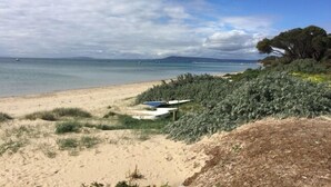 A beach with a sandy path leading to a small boat, surrounded by dense vegetation and a clear view of the sea and distant land. - Spacious Sorrento Retreat (Sorrento)