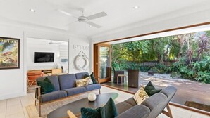 Un salon moderne avec un canapé, une table basse et un téléviseur. Une grande fenêtre offre une vue sur la verdure à l’extérieur.