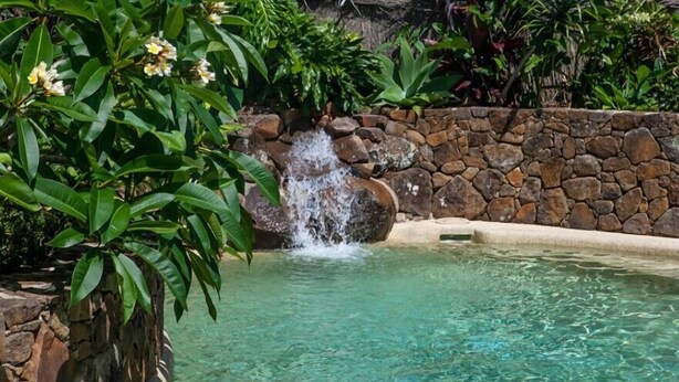 Une piscine aux eaux cristallines, bordée d’un mur de pierres et agrémentée d’une petite cascade.