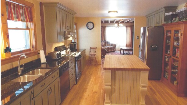 A kitchen with wooden cabinets, a stove, and a refrigerator. There is a dining table and a sofa in the adjacent living room.