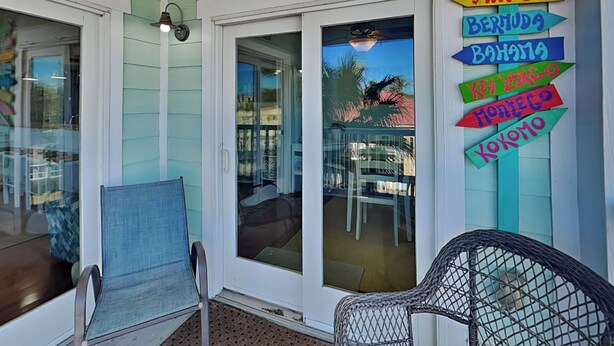 A room with a view of a balcony, a chair, and a signboard with destinations like Aruba, Jamaica, Bermuda, Bahamas, Key Largo, Montego Bay, and Cozumel. - Captains Watch 15 | Walk to Beach + Shops, Rooftop Community Pool (Tybee Island)
